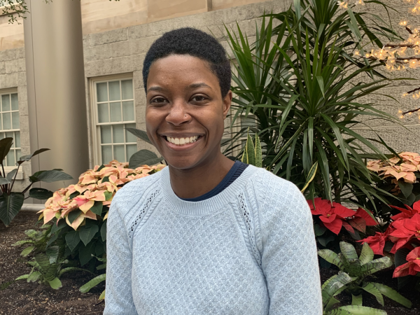 Ashleigh D. Coren sits, surrounded by red and yellow flowers, in the Kogod Courtyard. She smiles.