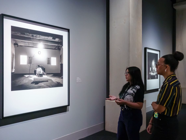 Two young women stand together, looking at a photograph displayed on the wall as part of the Smithsonian American Art Museum installation.