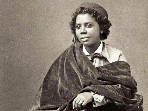 Edmonia Lewis, seated on a chair with tassels. 