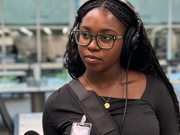 Lena DoDoo with headphones on and holding a microphone pointed towards someone out of frame. 