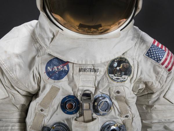 Color photograph of the upper torso and neck of Neil Armstrong's Apollo 11 spacesuit. A NASA patch is on the left and an Apollo 11 patch with an eagle on the moon is on the right.