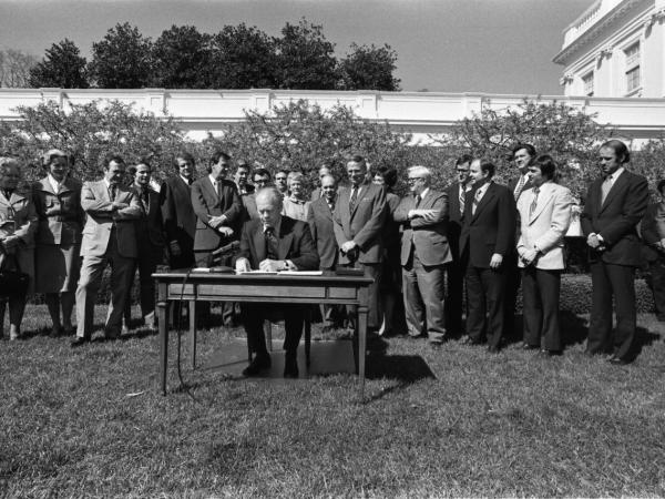 An image of President Ford signing the Equal Credit Opportunity Act on a table in a lawn surrounded by people.