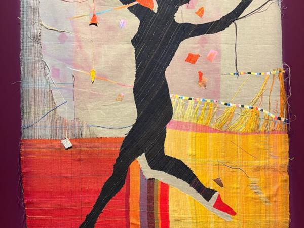 A black silhouette of a jumping woman against a colorful fabric background.  