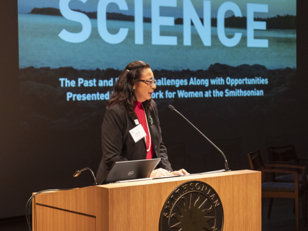 Oris Sanjur speaks at a podium. The words Women in Science are projected on a screen behind her.