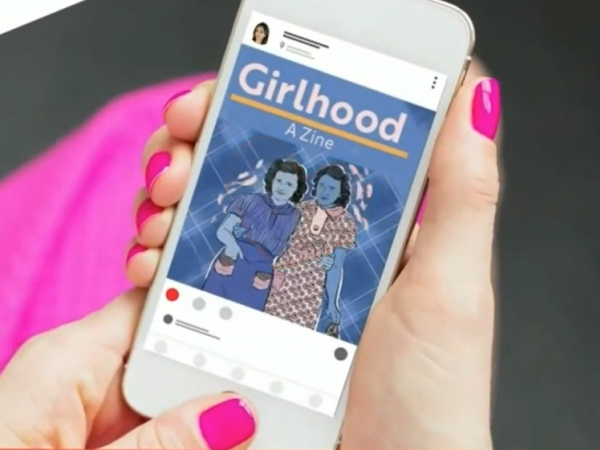 Hand with pink painted fingernails holding a cell phone. The screen shows an illustration of women and the text: Girlhood / A Zine