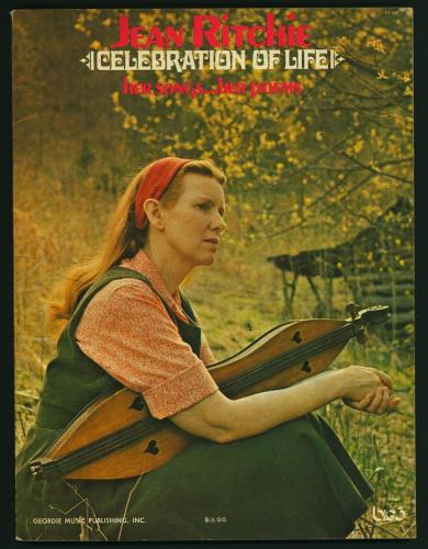Color photograph of Jean Ritchie holding a mountain dulcimer while sitting on a grassy hill.