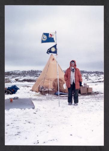 Ursula Marvin stands next to a tent and a flagpole with a Smithsonian sunburst flag in a snowy landscape