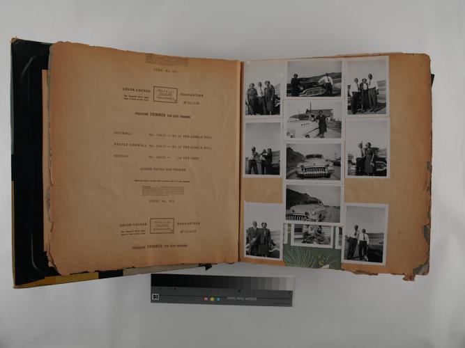 Color photograph of a large, opened book showing two pages. The left page has printed information about the wallpaper sample on the reverse side. The right page has 11 black and white snapshots of various people standing in front of automobiles. The center photograph is a front view of a 1950s sedan.  