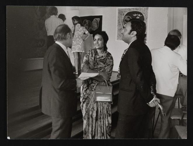 Zarina Hashmi talks with two men at a gallery, with other visitors view the art behind them
