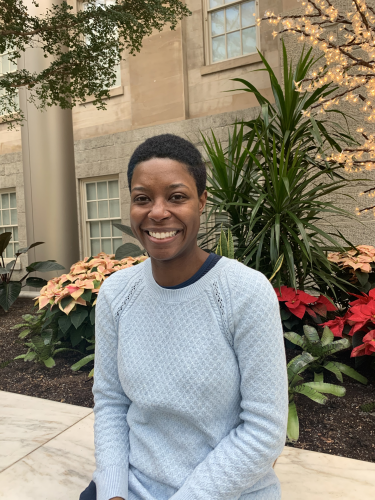 Ashleigh D. Coren sits, surrounded by red and yellow flowers, in the Kogod Courtyard. She smiles.