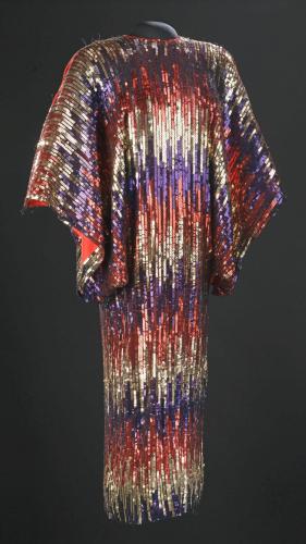 alt=&quot;Red, gold, and blue sequin dress designed with horizontal, varied stripes and large open sleeves.&quot;