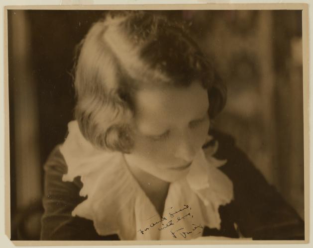 Sepia portrait of Edna St. Vincent Millay from the waist up. She is bent over and looking down at something of camera.   