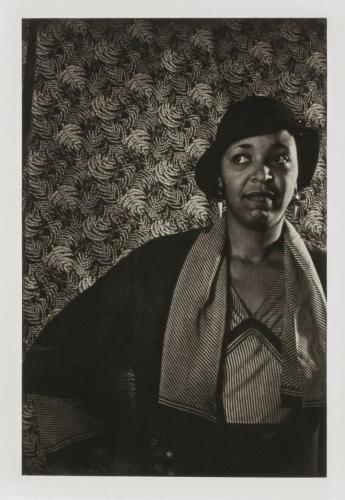 Ethel Waters stands with her hands on her hips, looking off-camera. She stands in front of an elaborately patterned background.