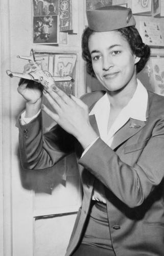 Ruth Carol Taylor wears her flight attendant uniform and holds a miniature plane model in the air