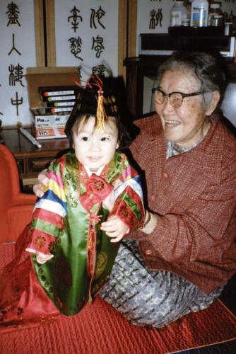 A color photo of Sung Hark (Lee) Kang sitting on a red carpet holding up Nicole as a toddler.