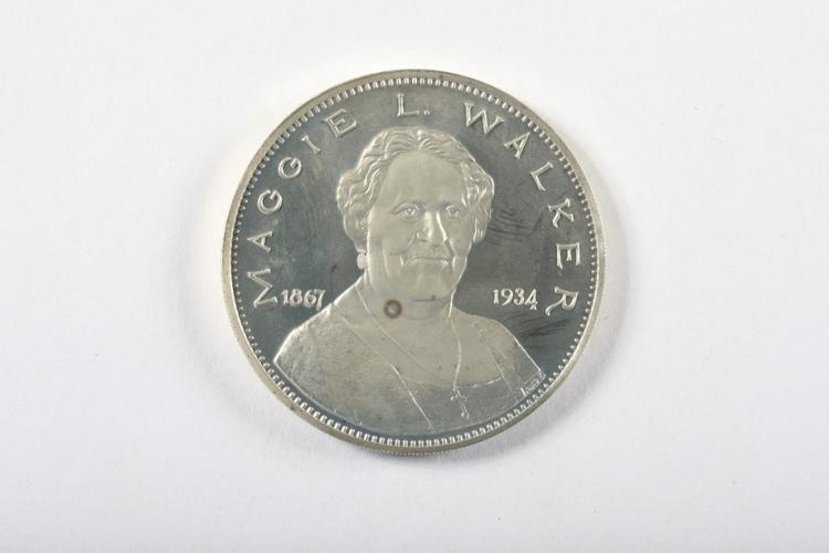 Round silver medal with the bust of Maggie Lena Walker on the front. The words “Maggie L. Walker” arch across the top with the dates 1867 and 1934 below. 