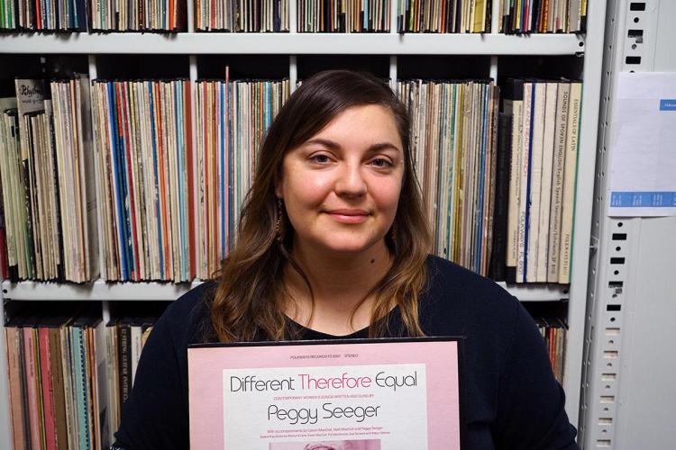 Meredith Holmgren holds a record that says "Different Therefore Equal / Peggy Sawyer. "She stands in front of a shelf full of records. 