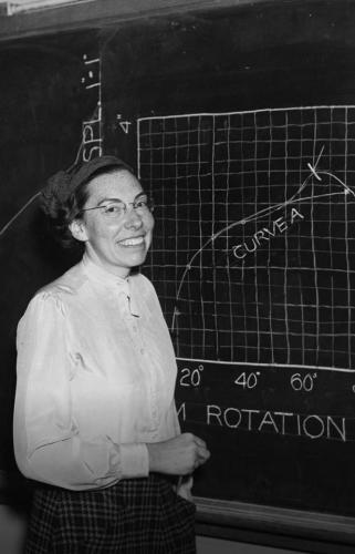 Mary Blade stands smiling in front of a chalkboard with a graph drawn on it