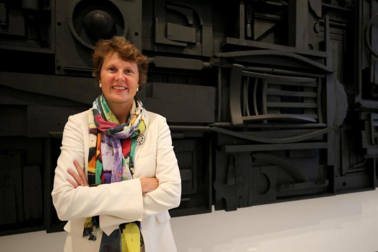 Stephanie Stebich stands in front of a wall-mounted artwork with wood objects painted black