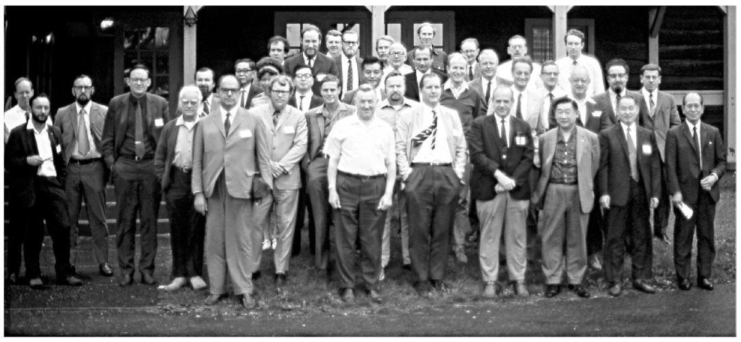 Group of men in suits stand together for a picture. The head of a woman can be seen in the second row.