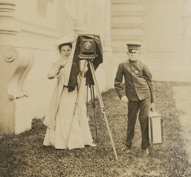 Photograph of a woman standing behind camera with man next to her 